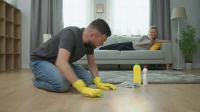 O tiro médio do homem limpa o assoalho de parquet, e as mentiras da mulher no sofá com o smartphone O tiro médio do homem limpa o assoalho de parquet, e as mentiras da mulher no sofá com o smartphone