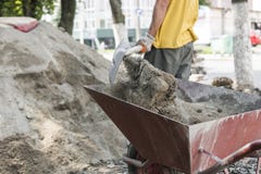 O uso do trabalhador a pá e enche o carrinho de mão com a areia para a construção da estrada do passeio Ferramentas da construção imagem de stock O uso do trabalhador a pá e enche o carrinho de mão com a areia para a construção da estrada do passeio Ferramentas da construção imagem de stock