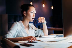 Occhiali asiatici pensierosi della tenuta della donna di affari ed esaminare il monitor del computer fotografie stock Occhiali asiatici pensierosi della tenuta della donna di affari ed esaminare il monitor del computer fotografie stock