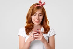Odosobniony strzał piękna uśmiechnięta imbirowa kobieta z powabnym uśmiechem, uses nowożytny telefon komórkowy, wiadomości z przy obrazy royalty free Odosobniony strzał piękna uśmiechnięta imbirowa kobieta z powabnym uśmiechem, uses nowożytny telefon komórkowy, wiadomości z przy obrazy royalty free