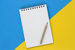 Offenes gewundenes Notizbuch mit einer Leerseite und einem Bleistift auf einem blauen und gelben Hintergrund, mit Kopienraum lizenzfreies stockfoto Offenes gewundenes Notizbuch mit einer Leerseite und einem Bleistift auf einem blauen und gelben Hintergrund, mit Kopienraum lizenzfreies stockfoto