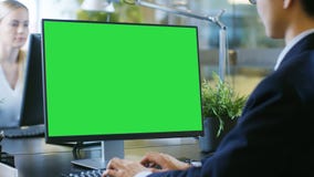 In the Office Businessman works at His Desk on a Personal Computer with Mock-up Green Screen. His Colleague Sets Opposite to Him. stock images In the Office Businessman works at His Desk on a Personal Computer with Mock-up Green Screen. His Colleague Sets Opposite to Him. stock images