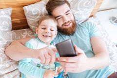 Ojcuje używać smartphone i lying on the beach na łóżku z małym synem obraz royalty free Ojcuje używać smartphone i lying on the beach na łóżku z małym synem obraz royalty free