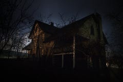 Old House With A Ghost In The Forest At Night Or Abandoned Haunted Horror House In Fog. Old Mystic Building In Dead Tree Forest. Royalty Free Stock Image