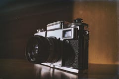 Old style retro analog film camera standing on the shelve with sun shining from the side stock photo Old style retro analog film camera standing on the shelve with sun shining from the side stock photo
