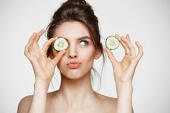 Olho escondendo de sorriso da menina despida bonita nova atrás da fatia do pepino sobre o fundo branco Termas e cosmetologia da b foto de stock Olho escondendo de sorriso da menina despida bonita nova atrás da fatia do pepino sobre o fundo branco Termas e cosmetologia da b foto de stock