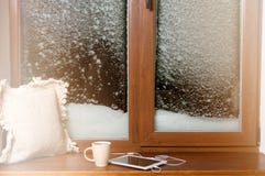 On The Windowsill Of A Snow-covered Window In Winter There Is A Cup Of Black Coffee And A Tablet With Headphones, A Pillow Is In Stock Photo