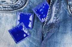 One condom in zipper and two condoms scattered on blue jeans stock photography One condom in zipper and two condoms scattered on blue jeans stock photography