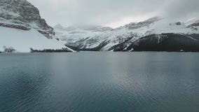Aerial footage of the surface of Bow Lake with snow-capped mountains in Alberta, Canada