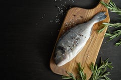 Op взгляд свежих сырцовых рыб dorada с розмариновым маслом, перцем и солью на деревянной доске и черной таблице стоковое изображение rf Op взгляд свежих сырцовых рыб dorada с розмариновым маслом, перцем и солью на деревянной доске и черной таблице стоковое изображение rf