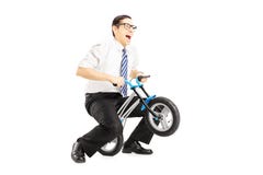 Opgewekte jonge zakenman die een kleine fiets berijdt stock fotografie Opgewekte jonge zakenman die een kleine fiets berijdt stock fotografie