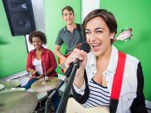 Opgewekte Vrouw die terwijl Band die Muzikaal Instrument spelen zingen stock afbeelding Opgewekte Vrouw die terwijl Band die Muzikaal Instrument spelen zingen stock afbeelding