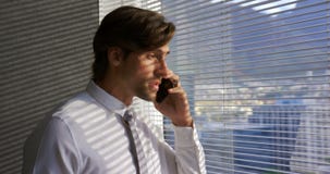 Opinião lateral o executivo masculino caucasiano novo que fala no telefone celular perto da janela no escritório moderno 4k filme Opinião lateral o executivo masculino caucasiano novo que fala no telefone celular perto da janela no escritório moderno 4k filme