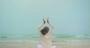Opinião traseira a mulher afro-americano superior ativa que faz a ioga na esteira do exercício na praia 4k video estoque Opinião traseira a mulher afro-americano superior ativa que faz a ioga na esteira do exercício na praia 4k video estoque
