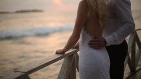 Opinión trasera la novia y el novio que disfrutan de puesta del sol en la playa tropical cerca de la barandilla el vacaciones Rec metrajes Opinión trasera la novia y el novio que disfrutan de puesta del sol en la playa tropical cerca de la barandilla el vacaciones Rec metrajes