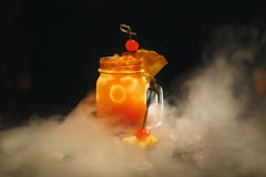 Orange de cocktail sur un fond noir Décoré de la cerise et entouré par la glace et la fumée photos stock Orange de cocktail sur un fond noir Décoré de la cerise et entouré par la glace et la fumée photos stock