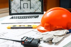Orange Schutzhelm, Laptop mit Zeichnungen, waagerecht ausgerichtetes Meter, Funksprechgerät und Handschuhe, die auf Pläne auf ein stockfoto Orange Schutzhelm, Laptop mit Zeichnungen, waagerecht ausgerichtetes Meter, Funksprechgerät und Handschuhe, die auf Pläne auf ein stockfoto