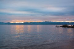 Orange sunset above hilly side of sea. Overcast sky and reflection on water Stock Image Orange sunset above hilly side of sea. Overcast sky and reflection on water Stock Image