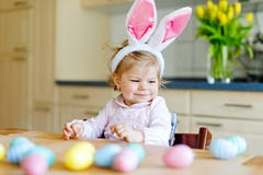 Orelhas vestindo do coelhinho da Páscoa da menina pequena bonito da criança que jogam com os ovos pasteis coloridos Criança feliz foto de stock Orelhas vestindo do coelhinho da Páscoa da menina pequena bonito da criança que jogam com os ovos pasteis coloridos Criança feliz foto de stock