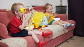 Os irmãos sentam-se no sofá em casa e olham-se a tevê Coma varas e sorriso do milho filme Os irmãos sentam-se no sofá em casa e olham-se a tevê Coma varas e sorriso do milho filme