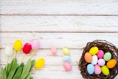Os ovos da páscoa coloridos no ninho com tulipa florescem no fundo de madeira rústico das pranchas Imagem de Stock Os ovos da páscoa coloridos no ninho com tulipa florescem no fundo de madeira rústico das pranchas Imagem de Stock