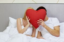 Os pares felizes na cama com forma vermelha do coração descansam imagem de stock Os pares felizes na cama com forma vermelha do coração descansam imagem de stock