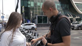 Os turistas, um homem e uma mulher, comunicam perto do planeamento alugado da bicicleta uma excursão da cidade video estoque Os turistas, um homem e uma mulher, comunicam perto do planeamento alugado da bicicleta uma excursão da cidade video estoque