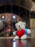 Ours de nounours blanc portant le coeur rouge de prise bleue de chemise et se reposant sur la table en bois devant l'espace de co Images libres de droits Ours de nounours blanc portant le coeur rouge de prise bleue de chemise et se reposant sur la table en bois devant l'espace de co Images libres de droits