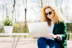 Outdoor portrait of attractive young girl with fluffy blonde hair wearing sunglasses, jeans and green jacket holding laptop comput stock images Outdoor portrait of attractive young girl with fluffy blonde hair wearing sunglasses, jeans and green jacket holding laptop comput stock images