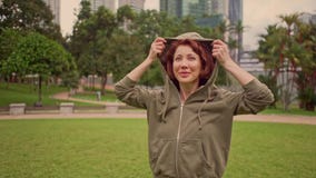Outdoors 360 degree gimbal shot on young attractive and fit woman putting on hoodie starting running at green city park stock footage Outdoors 360 degree gimbal shot on young attractive and fit woman putting on hoodie starting running at green city park stock footage