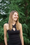 Outdoors Portrait of Attractive Smiling Woman in Black Shirt near Spruce Tree During Summer Time. stock photo Outdoors Portrait of Attractive Smiling Woman in Black Shirt near Spruce Tree During Summer Time. stock photo