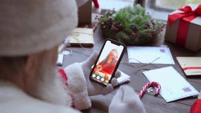 Santa Claus talking to child on phone video call open present sit at table.