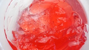 Overhead image of a glass bowl with strawberry jelly spinning on a white background
