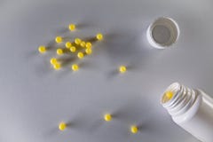Overhead shot of a spilled white pill bottle and small yellow balls on a gray background royalty free stock photography Overhead shot of a spilled white pill bottle and small yellow balls on a gray background royalty free stock photography
