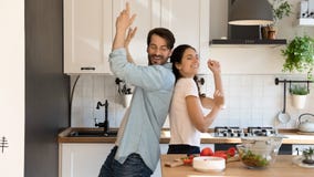 Overjoyed couple tenants dance in kitchen cooking together