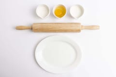 Ovo, farinha, leite, pino do rolo de madeira e placa branca no fundo branco foto de stock Ovo, farinha, leite, pino do rolo de madeira e placa branca no fundo branco foto de stock