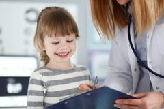 Paciente lindo que escucha del doctor de sexo femenino peque?o y escritura de la informaci?n del registro en el coj?n del tablero imagen de archivo libre de regalías Paciente lindo que escucha del doctor de sexo femenino peque?o y escritura de la informaci?n del registro en el coj?n del tablero imagen de archivo libre de regalías