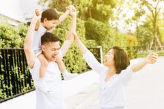 Padre asiático lindo que lleva a cuestas a su hijo junto con su esposa en el parque Familia emocionada que aumenta las manos así imagen de archivo Padre asiático lindo que lleva a cuestas a su hijo junto con su esposa en el parque Familia emocionada que aumenta las manos así imagen de archivo