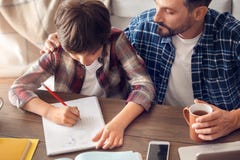 Padre e figlio a casa che si siedono al tè bevente del papà della tavola che tocca spalla complementare del ragazzo che fa eserci fotografie stock libere da diritti Padre e figlio a casa che si siedono al tè bevente del papà della tavola che tocca spalla complementare del ragazzo che fa eserci fotografie stock libere da diritti