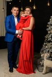 Pai com mãe e sua posição da filha ao lado de uma mamã da árvore de Natal com a filha em vestidos vermelhos imagem de stock Pai com mãe e sua posição da filha ao lado de uma mamã da árvore de Natal com a filha em vestidos vermelhos imagem de stock