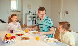 Pai feliz com suas crianças que falam no café da manhã em casa foto de stock Pai feliz com suas crianças que falam no café da manhã em casa foto de stock