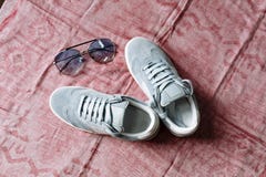 A pair of blue suede sneakers on a white sole with white accents and sunglasses with blue glasses on a pink background royalty free stock image A pair of blue suede sneakers on a white sole with white accents and sunglasses with blue glasses on a pink background royalty free stock image
