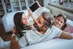 Pais que sentam-se no sofá com filha e que clicam um selfie na tabuleta digital imagem de stock royalty free Pais que sentam-se no sofá com filha e que clicam um selfie na tabuleta digital imagem de stock royalty free