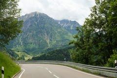 Paisagem idílico da montanha com uma estrada na parte dianteira e as montanhas no fundo imagens de stock Paisagem idílico da montanha com uma estrada na parte dianteira e as montanhas no fundo imagens de stock