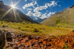 Paisaje de la cordillera con el valle verde iluminado por la luz del sol, el cielo azul con las nubes y un pequeño canal de agua imagen de archivo libre de regalías Paisaje de la cordillera con el valle verde iluminado por la luz del sol, el cielo azul con las nubes y un pequeño canal de agua imagen de archivo libre de regalías