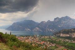 Panorama della polizia del lago, del villaggio Torbole della riva del lago e delle montagne con le nuvole di tempesta scure, Ital Fotografie Stock Panorama della polizia del lago, del villaggio Torbole della riva del lago e delle montagne con le nuvole di tempesta scure, Ital Fotografie Stock