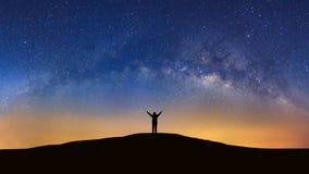 Panorama landscape with milky way, Night sky with stars and silhouette of a standing sporty man with raised up arms on high mount
