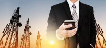 Panorama- står högt affärsmannen som använder mobiltelefonen med telekommunikation, med TVantenner och den satellit- maträtten i royaltyfri bild Panorama- står högt affärsmannen som använder mobiltelefonen med telekommunikation, med TVantenner och den satellit- maträtten i royaltyfri bild