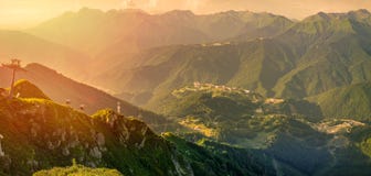 Panoramautsikten av solnedgången i sommar uppifrån av det Aibga området till skidar semesterorten Rosa Khutor Kabelbilen är arkivfoto Panoramautsikten av solnedgången i sommar uppifrån av det Aibga området till skidar semesterorten Rosa Khutor Kabelbilen är arkivfoto