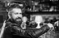 Pantaloni a vita bassa che si rilassano alla barra con birra L'uomo barbuto dei pantaloni a vita bassa brutali si siede alla birr immagine stock Pantaloni a vita bassa che si rilassano alla barra con birra L'uomo barbuto dei pantaloni a vita bassa brutali si siede alla birr immagine stock